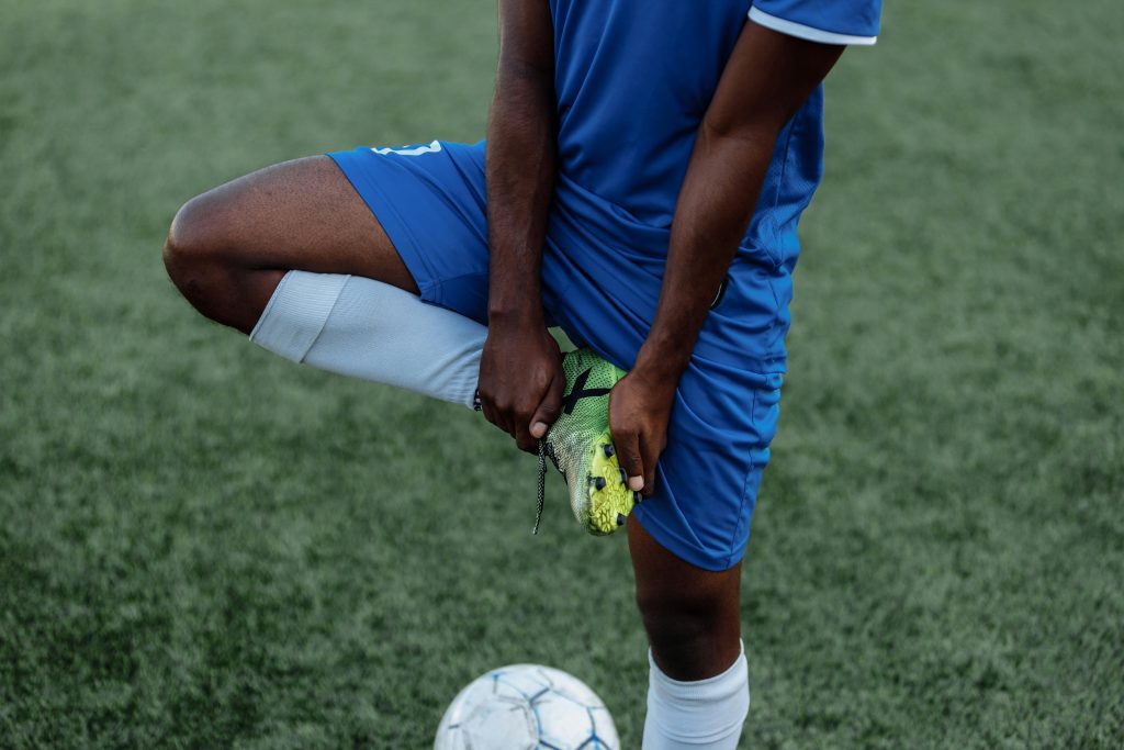 pexels-photo-5247207-5247207 A soccer player in a blue uniform stretches on the grassy field, preparing for the game.