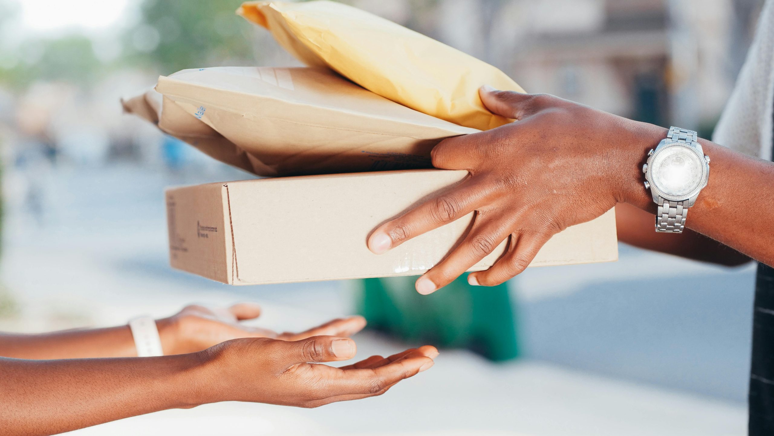 Close-up image of hands exchanging packages outdoors. Represents delivery and shipping services.